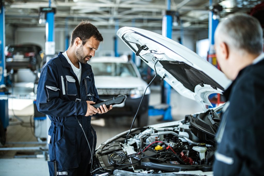 Auto mechanic working with car diagnostic tool in a repair shop.